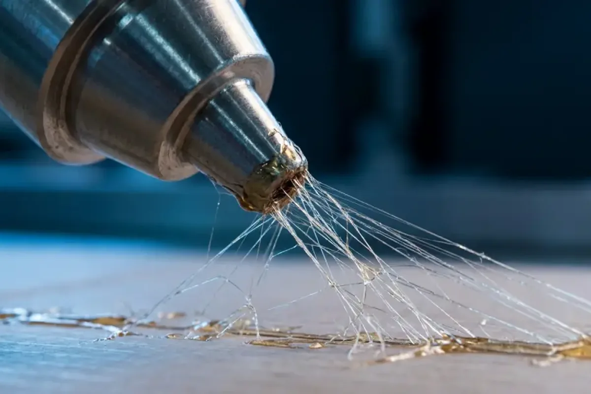Hot-melt nozzle pulling fine adhesive strings during an angel-hair defect check.