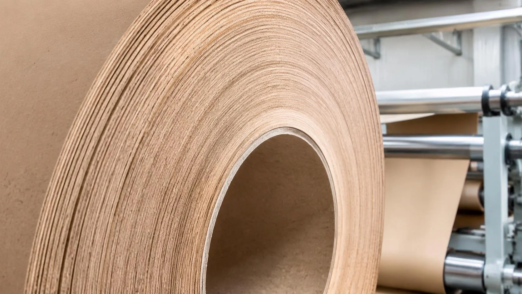 Close-up of a multi-ply kraft paper tube roll beside paper converting machinery.